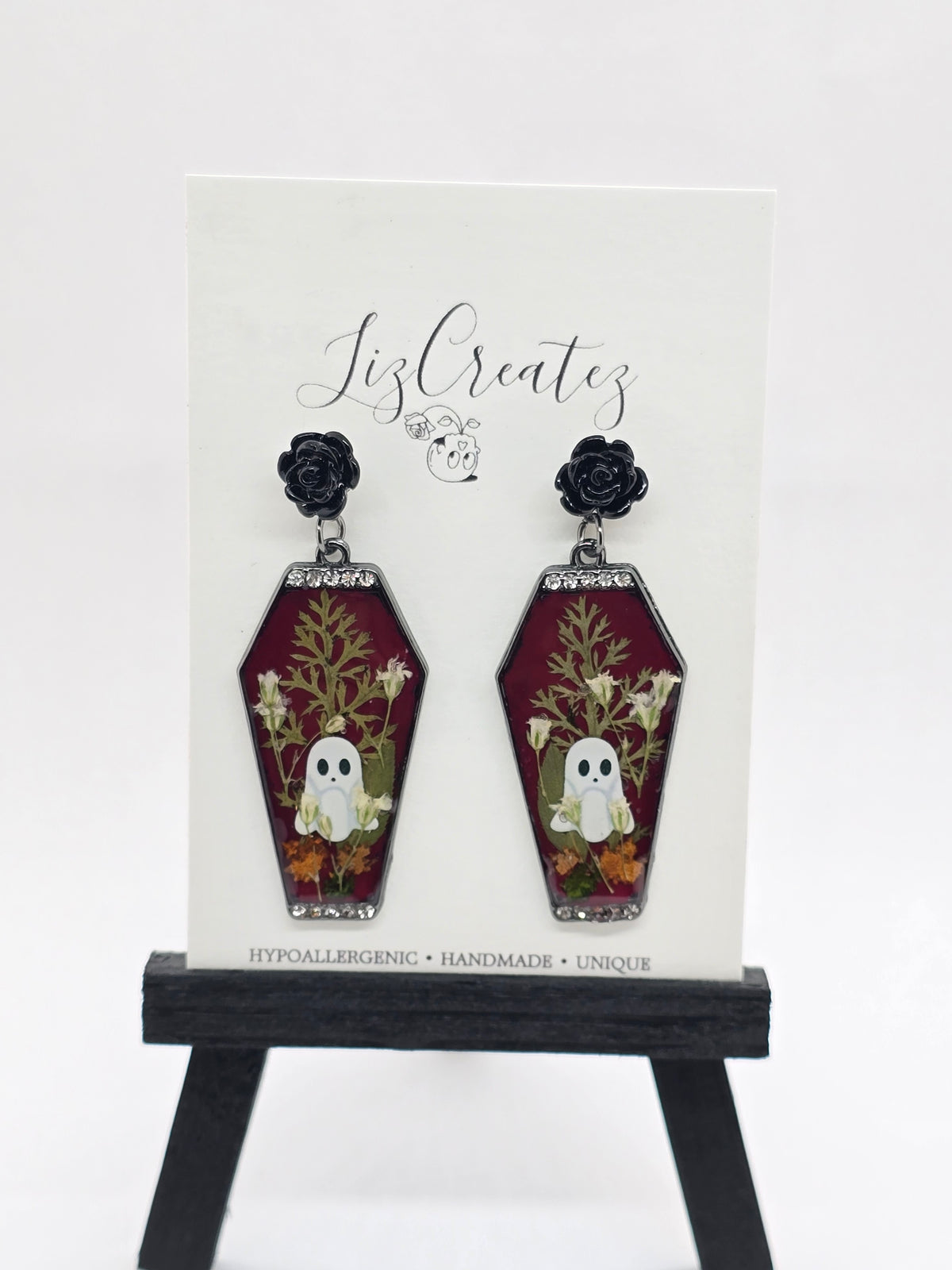 Coffin-shaped earrings with pressed flowers, a ghost design, black rose studs, and rhinestone trim, displayed on a LizCreatez card