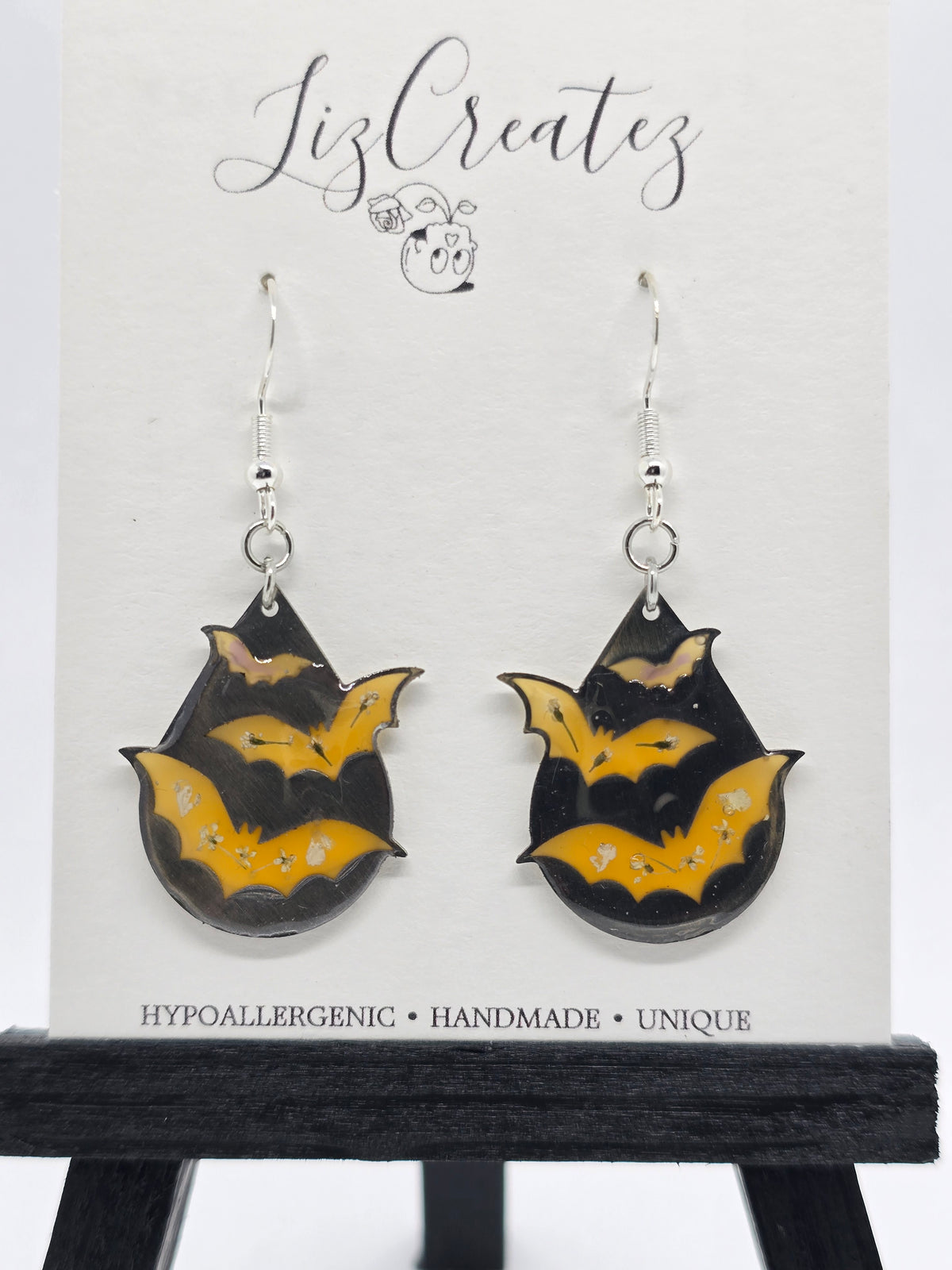 Bat-shaped earrings in orange colored resin with real flower accents, set in a silver open-back bezel on silver ear wires