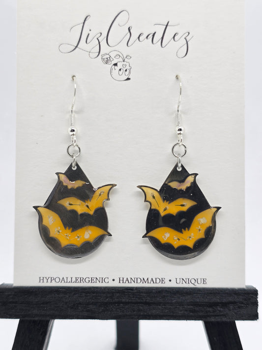 Bat-shaped earrings in orange colored resin with real flower accents, set in a silver open-back bezel on silver ear wires